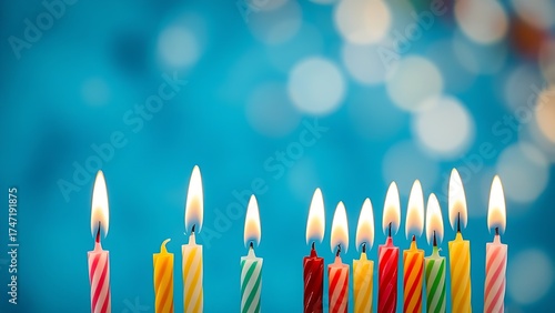 A row of colorful birthday candles flicker softly against a blurred blue backdrop.