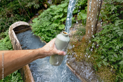 Картината върху платно Hand holding a reusable water bottle, refilling it with fresh, flowing water fro
