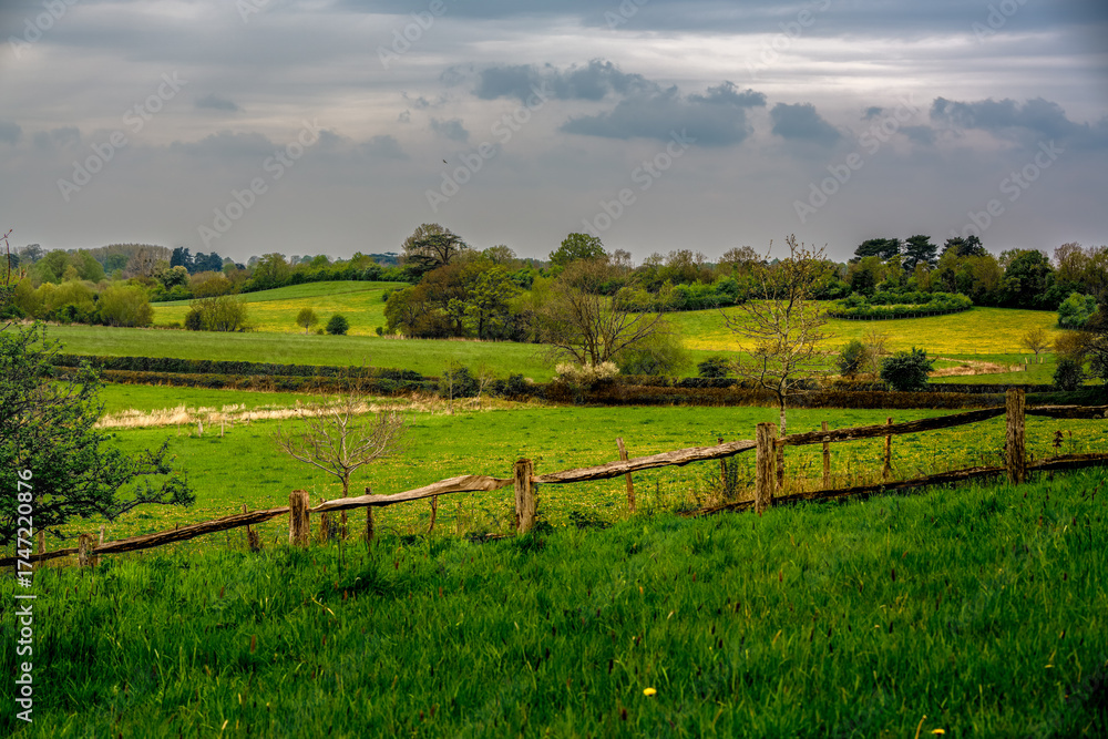 Obraz premium Peaceful English Countryside Landscape with Rolling Green Hills and Rustic Wooden Fence under Cloudy Sky