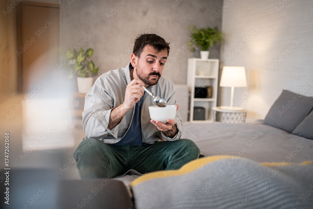 Fototapeta premium Man eating cereal in bed feeling lonely