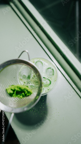 A green drink matcha is poured into a cup with a mesh strainer