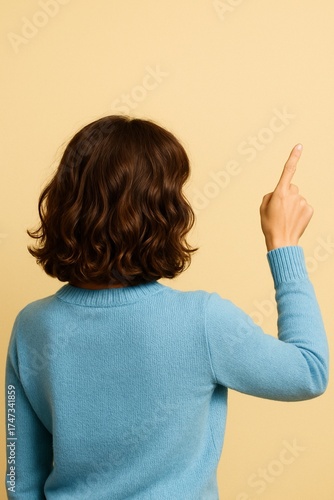 Chica de pelo castaño y ondulado de espaldas señalando arriba con el dedo.