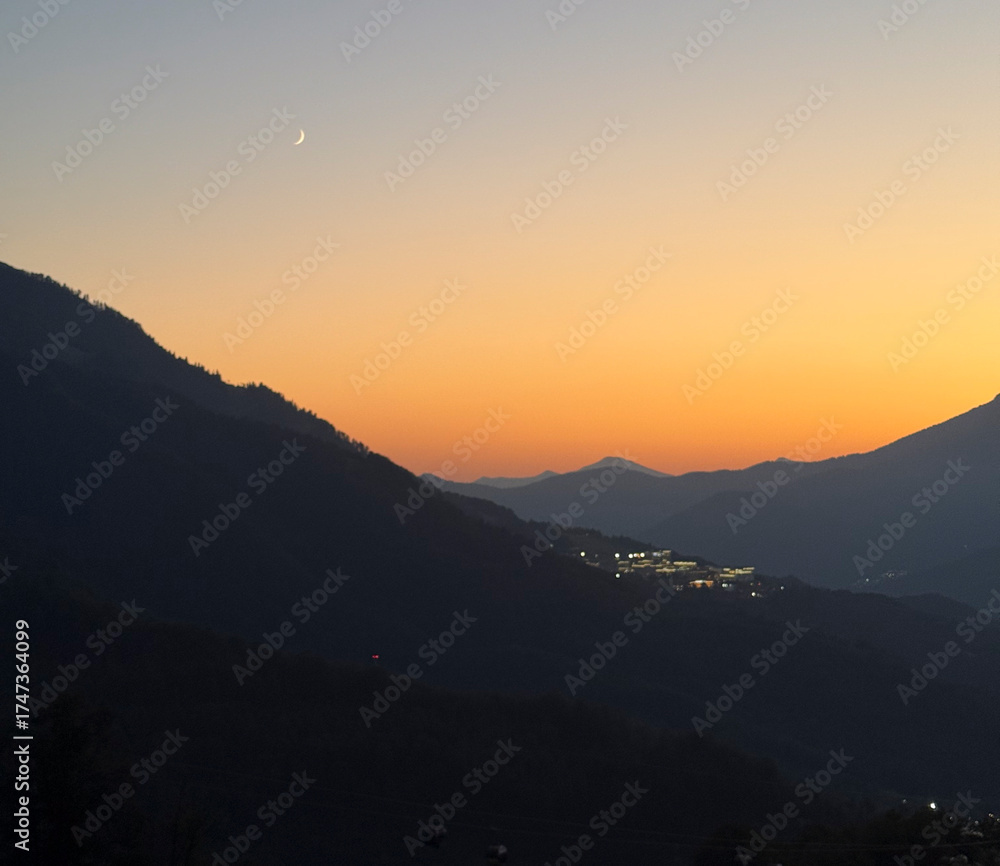 Obraz premium A beautiful sunset casts warm colors over the mountains as a crescent moon appears in the sky