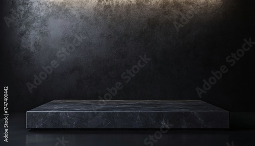 Fototapeta Naklejka Na Ścianę i Meble -  A single, dark gray marble block sits on a dark surface in front of a dark wall with subtle texture and a light gradient at the top.