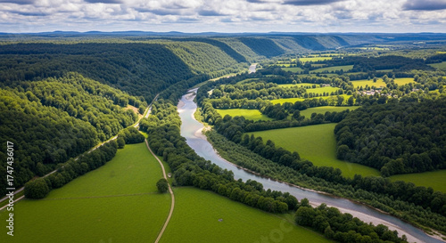 Aerial view of a lush green valley with a winding river flowing through it on a sunny day, creating a picturesque and tranquil landscape