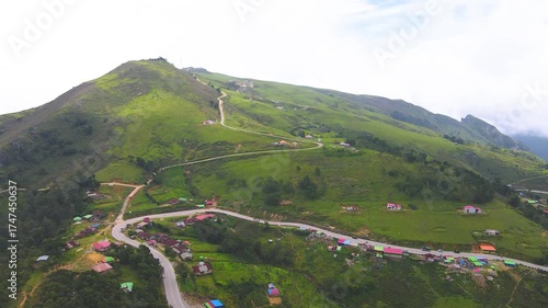 A dramatic aerial view of a mountain village in Flesha, Ainaro, Timor-Leste. Houses are scattered along a winding road that climbs up the vast, green mountain ridge