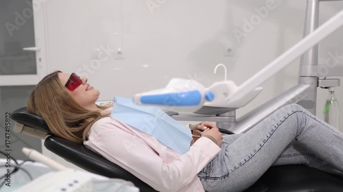 Woman relaxing in dental chair wearing protective glasses during dental treatment.