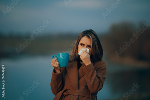 Woman Blowing her Nose Drinking Herbal tea During Cold Autumn. person suffers from influenza symptoms trying natural remedies