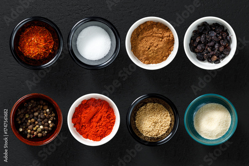 Spices and seasonings in small bowls on dark background, top view.