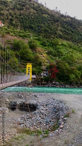 A panoramic view and close-up perspective of a vibrant yellow suspension bridge crossing the turquoise Swat River, framed by the lush, towering mountains of Khyber Pakhtunkhwa, Pakistan.