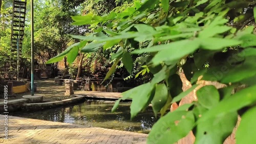 Tranquil stone pool surrounded by brick walls and lush green trees reflecting on clear water in peaceful sunlight.