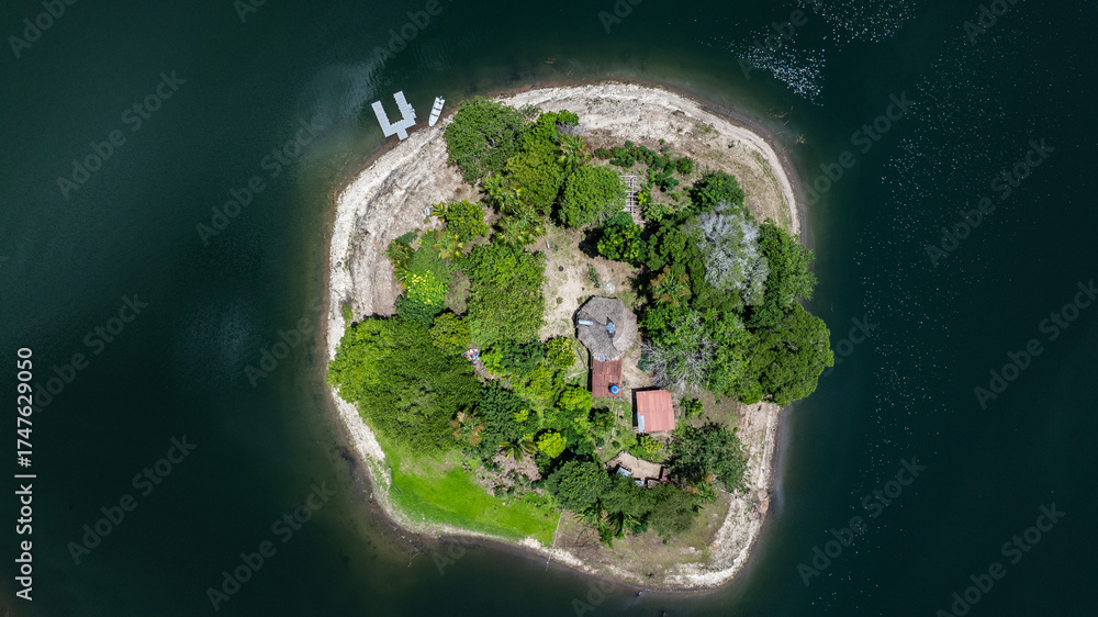 Fototapeta premium aerial top view of a round island with trees, hut building in the center, a jetty and small boat at shoreline, somewhere in the tropical travel destination 