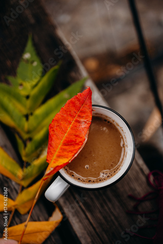 White mug of steaming coffee on burgundy fabric with autumn leaves. Warm colors and hygge fall atmosphere.