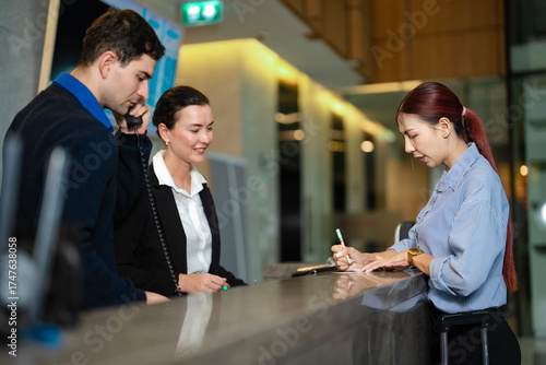 Friendly hotel front desk staff helping foreign with booking and payment, showing modern hospitality, digital system, and global tourism communication.