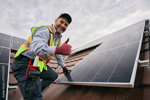 Tableau sur toile Happy worker showing thumb up while installing solar panels on roof and looking