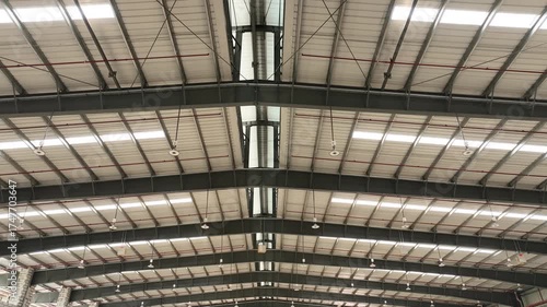 Spacious industrial warehouse interior. exposed steel beams, metal roof panels, bright overhead lighting. organized space. architectural symmetry and utilitarian design for storage and logistics