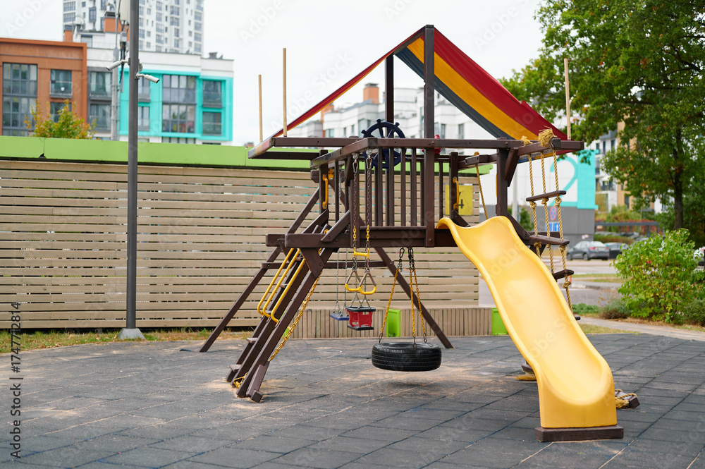 Fototapeta premium colorful playground with slide and climbing equipment in urban park setting. wooden play structure featuring vibrant yellow slide and tire swing, inviting play and enjoyment for children