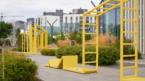 modern outdoor fitness equipment in urban park surrounded by greenery and contemporary architecture, featuring bright yellow structures under cloudy sky, promoting active urban lifestyle