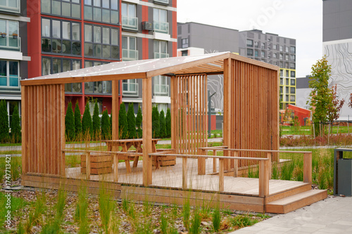 modern wooden gazebo in urban residential setting provides perfect outdoor seating area for relaxation and social gatherings. surrounded by green landscaping and vibrant apartment buildings