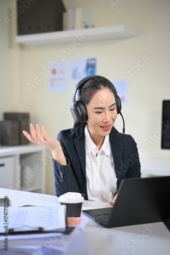 Asian woman customer service agent using laptop and microphone headset to assist clients with inquiries