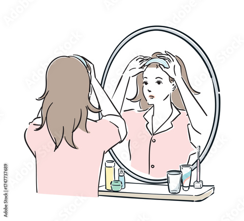 鏡の前でヘアバンドを止めるパジャマ姿の女性
