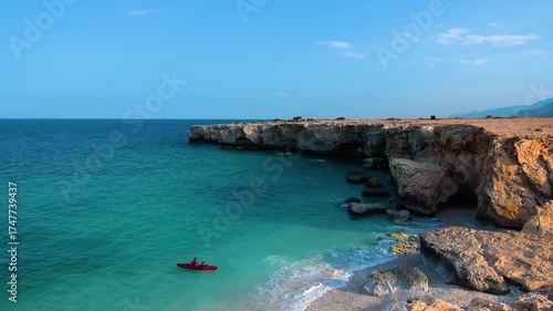 A person in a red kayak paddles peacefully along the beautiful turquoise waters and rugged cliffs of Fins Beach, a popular destination in the Sultanate of Oman.