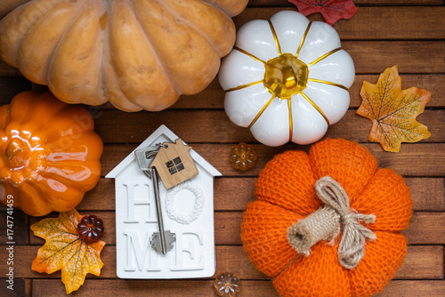 Cozy layout on a wooden background of slats with pumpkins, autumn leaves, a tiny house and keys - autumn mood, Halloween, housing, relocation, mortgage, insurance.