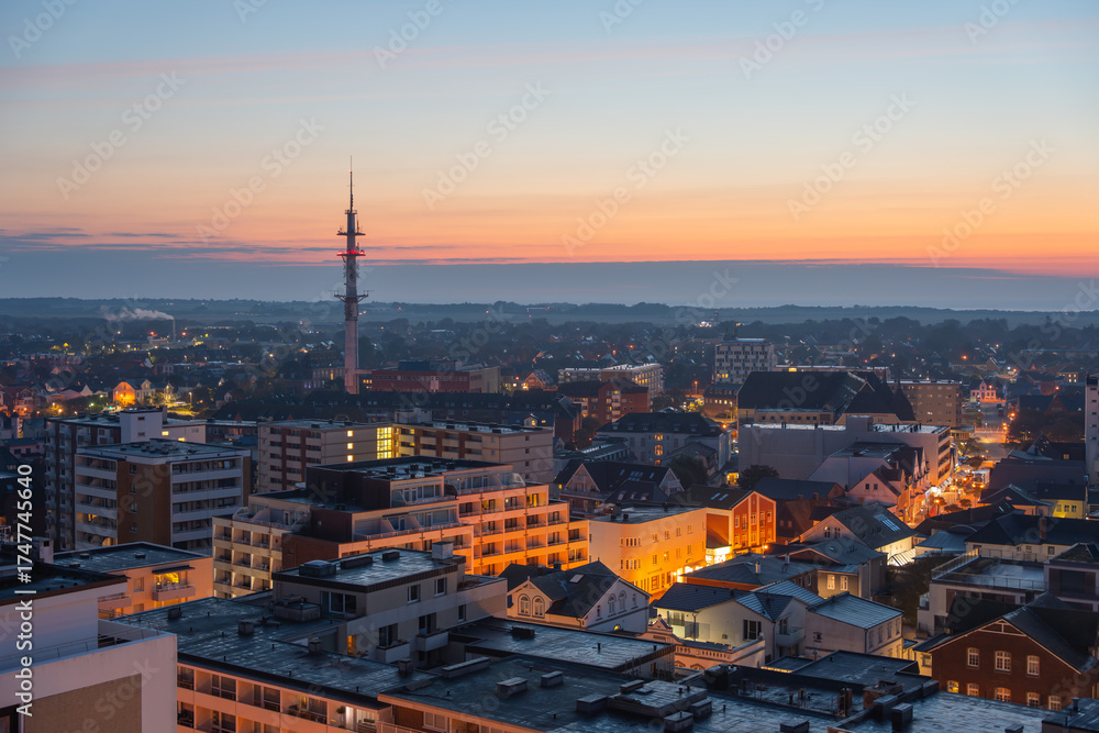 Naklejka premium A panoramic view of the city with a tall communications tower at sunset. Warm orange light contrasts with urban rooftops.