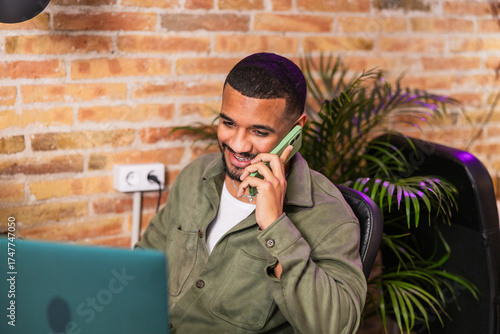 Young man working from home office talking on phone and smiling