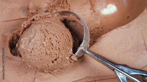 Balls of chocolate ice cream are slowly placed on a spoon and removed from the container.