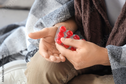 Foto Ill young man taking throat lozenges on sofa at home, closeup