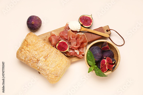 Fototapeta Naklejka Na Ścianę i Meble -  Wooden board with delicious prosciutto slices, ciabatta and bowl of fresh figs on beige background