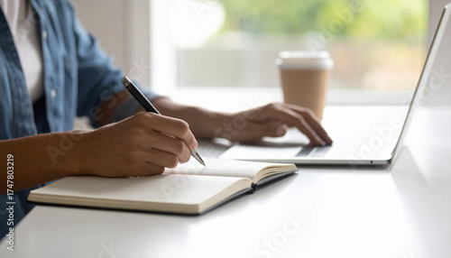 A person diligently working on a laptop and writing in a notebook, with a cup of coffee nearby, symbolizing productivity and focus