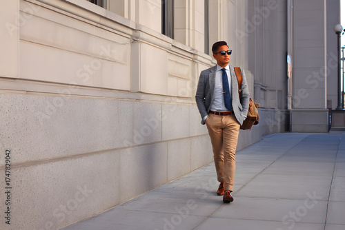 Urban Stroll of a Professional: A well-dressed individual strides confidently along the sidewalk beside a grand building, embodying urban sophistication and professional demeanor.