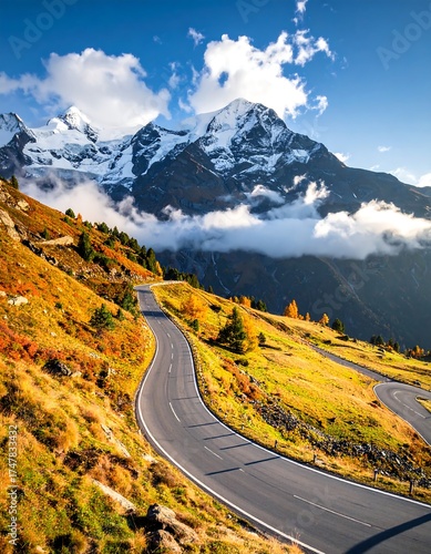 Winding road ascends a hillside, mountains in the background, sunny day