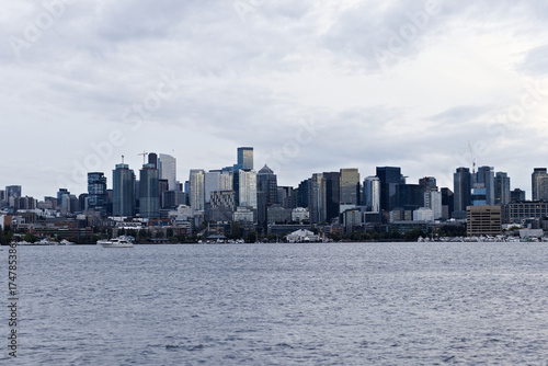 Downtown skyline view with tall buildings and boats on calm water under a cloudy sky, showcasing urban development and modern architecture.