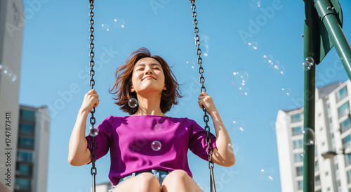 A happy young woman swings joyfully, smiling radiantly as whimsical bubbles dance around her under a clear blue sky, embodying pure freedom and carefree summer happiness