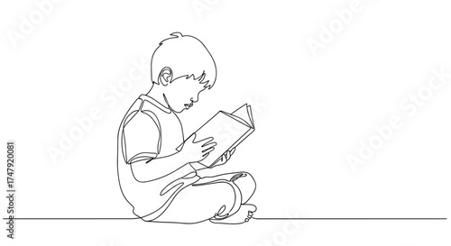 A young child is sitting cross-legged while engrossed in reading a book.