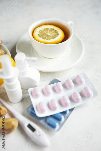 Cold and flu season treatment still life with cup of tea, lemon, pills, thermometer, nasal sprays, garlic and ginger, health and wellness concept