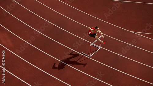 Aerial view of athlete jumping over hurdle on red running track with shadow. Concept of speed, discipline, determination for sports branding, motivation design, and athletic advertising visuals.