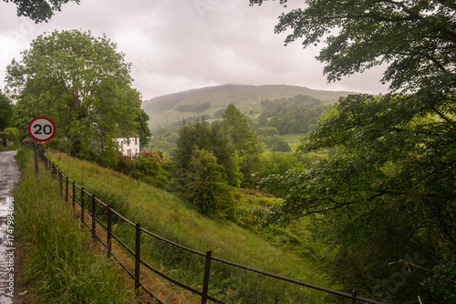 Landscape with trees, a road with raindrops on a guard rail and a speed limit traffic sign in Troutbeck, Cumbria, England