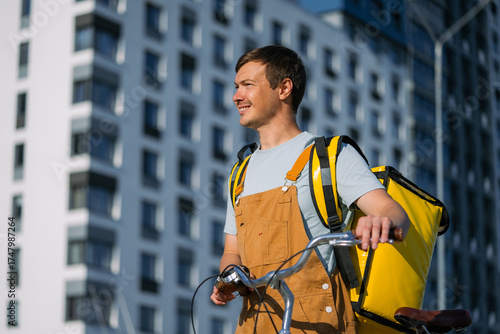 Tableau sur toile Happy bike courier working in the city, carrying a bright yellow delivery bag an