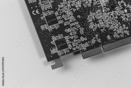 Monochrome macro photo of a black printed circuit board. The image highlights the complexity of microelectronics, showing chips, traces, and surface-mount components.

