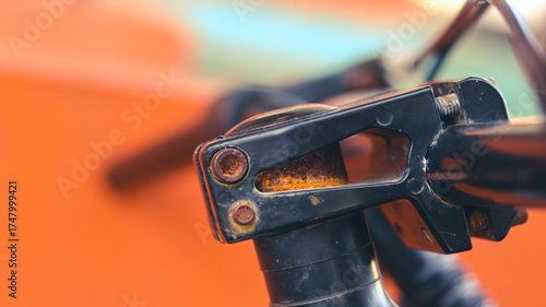 Close-up of rusted bicycle stem and handlebar clamp against orange background.