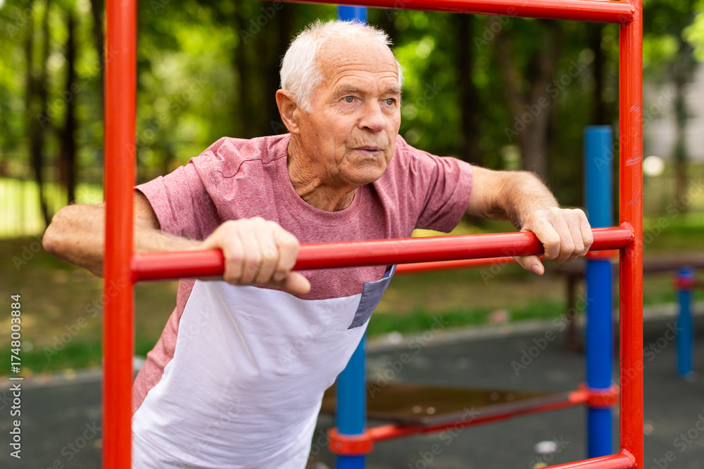 Obraz premium Elderly man doing fitness on sports ground equipment in park
