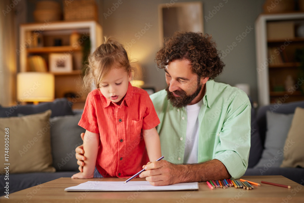 Naklejka premium A father and his young child focus on drawing together at home. The child stands by the table, excitedly creating art while the father guides and supports lovingly.
