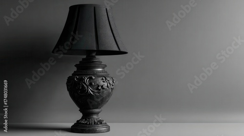 A vintage black table lamp with intricate carvings on its base sits on a flat surface against a gradient gray background. The lampshade has a textured, mosaic like appearance.