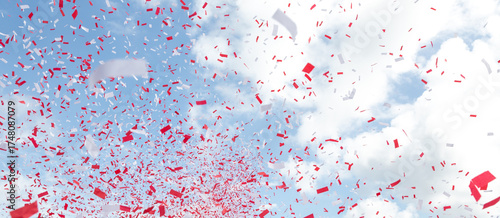 Red and white confetti against a blue sky with clouds