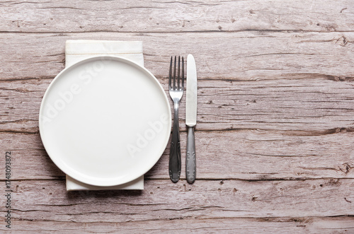 White plate, fork, knife and a napkin on wooden background with copy space.