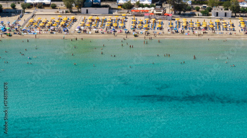 Aerial view of beach resorts and beach clubs with umbrellas and people vacationing on Mondello Beach, located near Palermo, Sicily, Italy. The turquoise water of the Tyrrhenian Sea in the foreground.